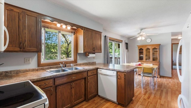 kitchen with a wealth of natural light, dark countertops, a sink, white appliances, and a peninsula