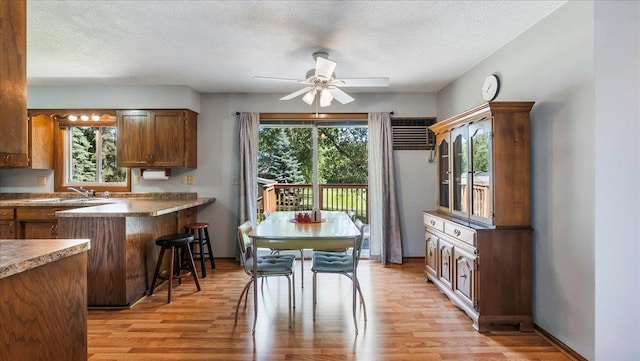 kitchen featuring a textured ceiling, light wood-style flooring, a peninsula, a kitchen breakfast bar, and brown cabinetry