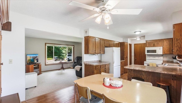 kitchen featuring a textured ceiling, a peninsula, white appliances, a sink, and brown cabinets