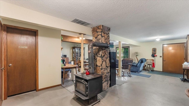 interior space with a wood stove, finished concrete floors, visible vents, and a textured ceiling