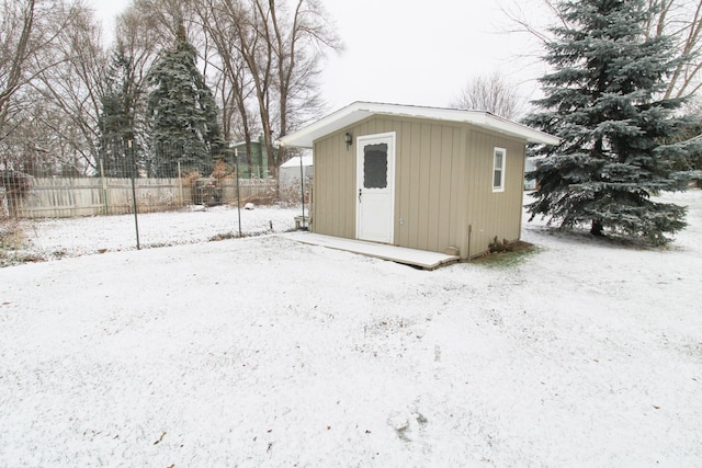 snow covered structure with a shed, an outdoor structure, and fence