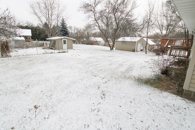 yard layered in snow featuring a garage, a shed, an outdoor structure, and a wooden deck