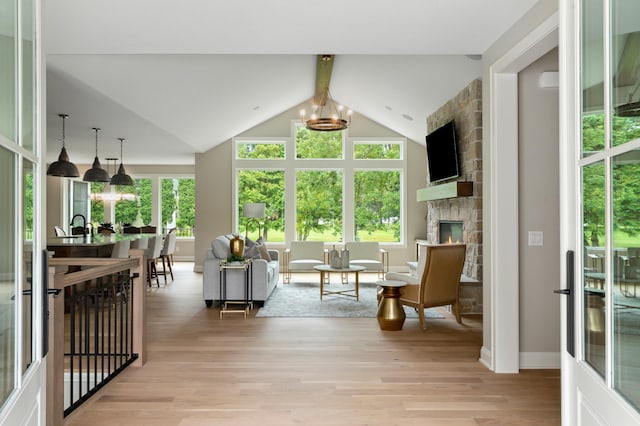 sunroom with a chandelier, lofted ceiling with beams, a stone fireplace, and plenty of natural light