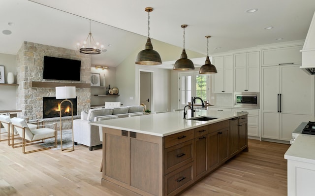 kitchen featuring stainless steel microwave, sink, a stone fireplace, decorative light fixtures, and white cabinets