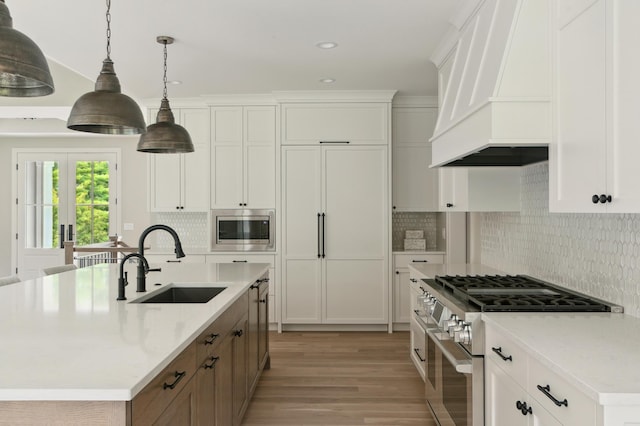 kitchen featuring a kitchen island with sink, white cabinets, sink, custom range hood, and stainless steel appliances