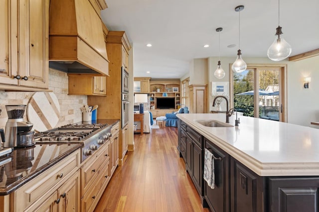 kitchen with custom range hood, decorative light fixtures, a center island with sink, and light wood-type flooring