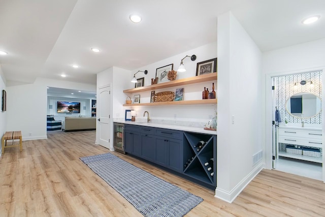 bar with sink, light wood-type flooring, and beverage cooler