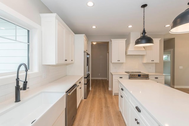 kitchen with white cabinetry, light hardwood / wood-style floors, decorative light fixtures, sink, and premium appliances