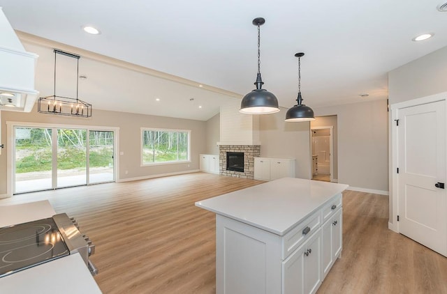 kitchen featuring white cabinets, hanging light fixtures, a kitchen island, a brick fireplace, and light hardwood / wood-style flooring