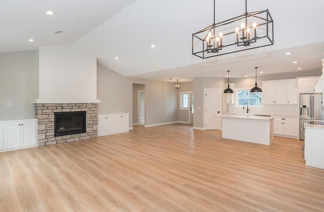 unfurnished living room featuring high vaulted ceiling, sink, a stone fireplace, light hardwood / wood-style floors, and a notable chandelier