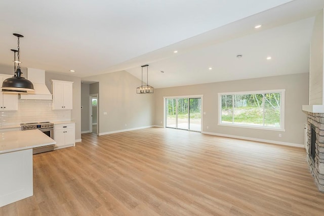 kitchen with stainless steel electric range, white cabinets, light wood-type flooring, vaulted ceiling, and a fireplace