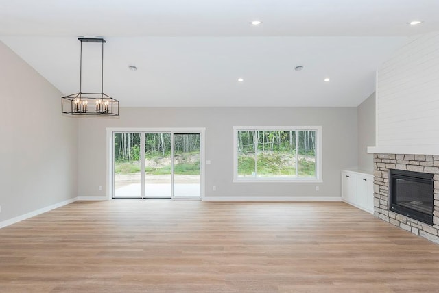 unfurnished living room featuring a wealth of natural light, a notable chandelier, a fireplace, and light wood-type flooring