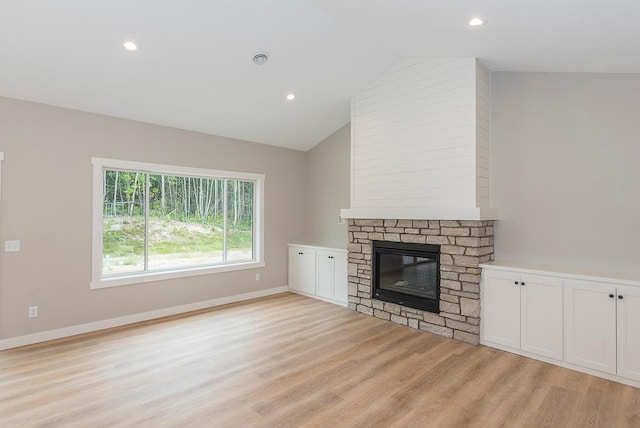 unfurnished living room with light hardwood / wood-style floors, lofted ceiling, and a stone fireplace