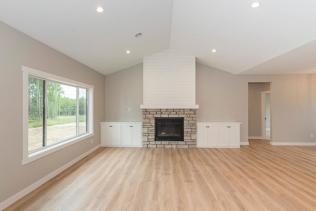 unfurnished living room with vaulted ceiling, a stone fireplace, and light wood-type flooring