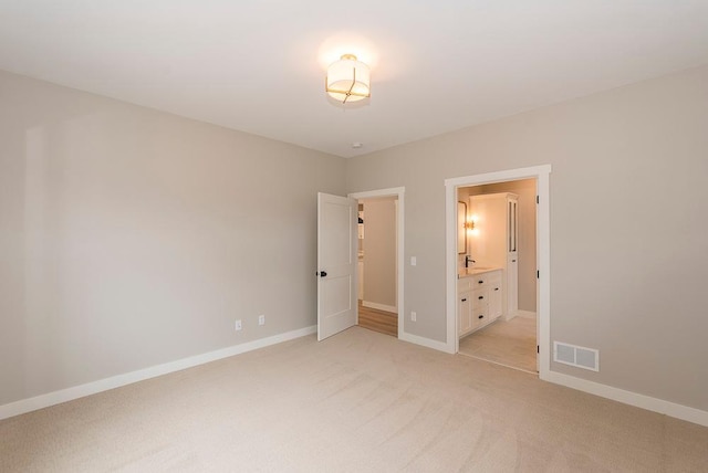 unfurnished bedroom featuring light colored carpet and ensuite bath