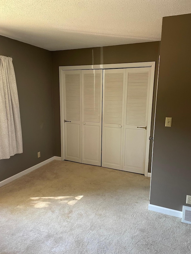 unfurnished bedroom featuring a closet, a textured ceiling, and light colored carpet