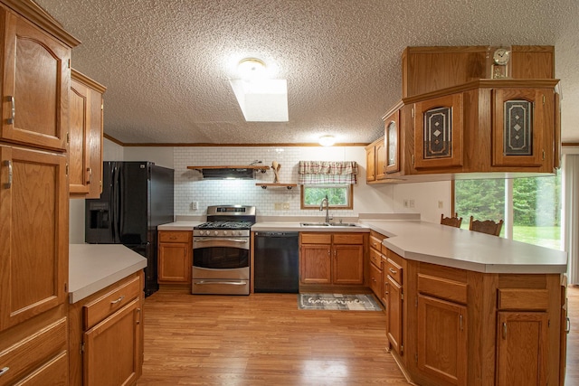 kitchen featuring a peninsula, a sink, light countertops, light wood-type flooring, and black appliances