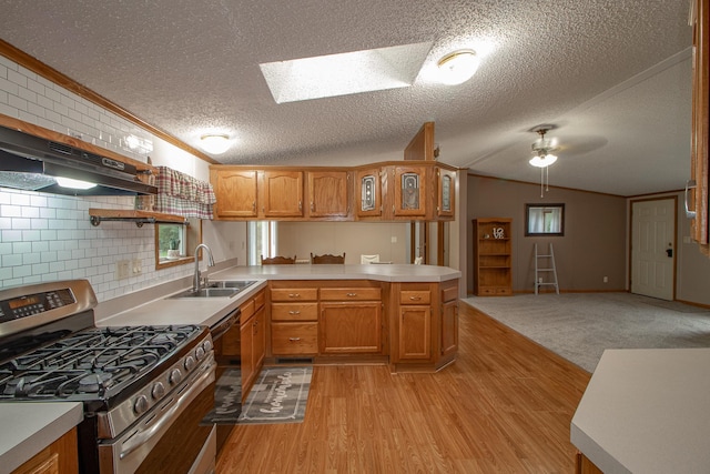 kitchen featuring vaulted ceiling with skylight, under cabinet range hood, a peninsula, a sink, and stainless steel gas range