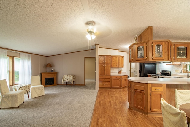 kitchen with a fireplace, light countertops, ornamental molding, brown cabinetry, and vaulted ceiling