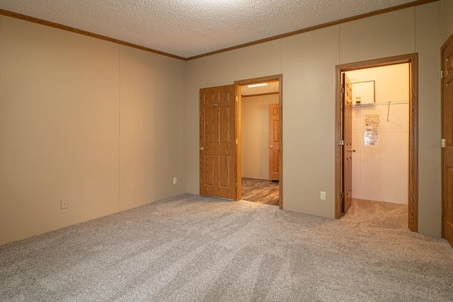 unfurnished bedroom with a textured ceiling, a spacious closet, carpet flooring, and crown molding