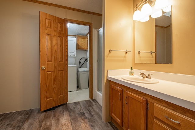 bathroom with stacked washer and clothes dryer, an enclosed shower, a textured ceiling, vanity, and wood finished floors