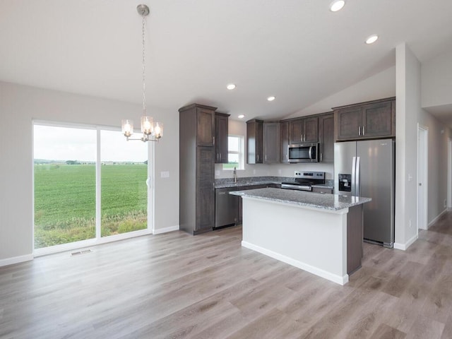 kitchen with light stone counters, stainless steel appliances, vaulted ceiling, a center island, and hanging light fixtures