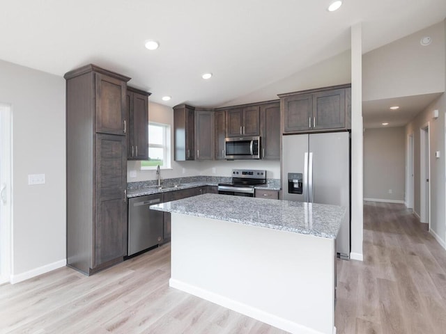 kitchen featuring lofted ceiling, a kitchen island, light stone countertops, appliances with stainless steel finishes, and light hardwood / wood-style floors