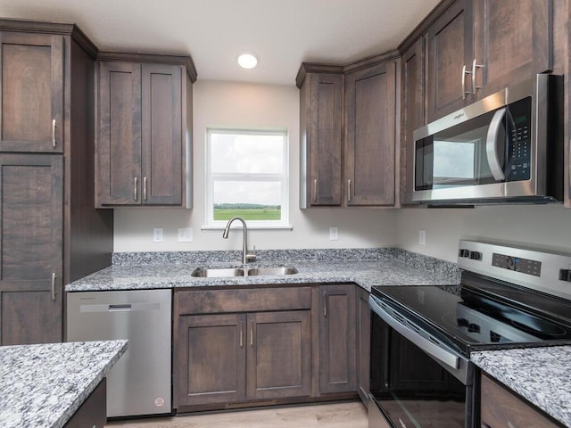 kitchen featuring dark brown cabinets, light stone countertops, sink, and appliances with stainless steel finishes