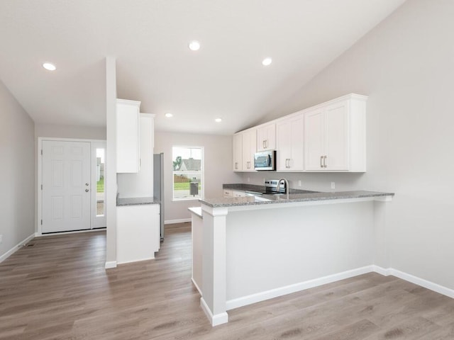 kitchen with stainless steel appliances, white cabinetry, vaulted ceiling, light wood-type flooring, and a peninsula