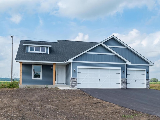 view of front of house with a garage, stone siding, roof with shingles, and driveway