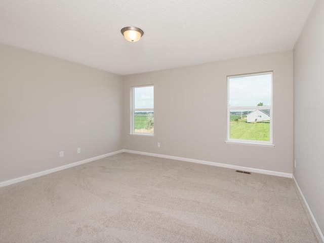 empty room featuring visible vents, light carpet, baseboards, and a textured ceiling