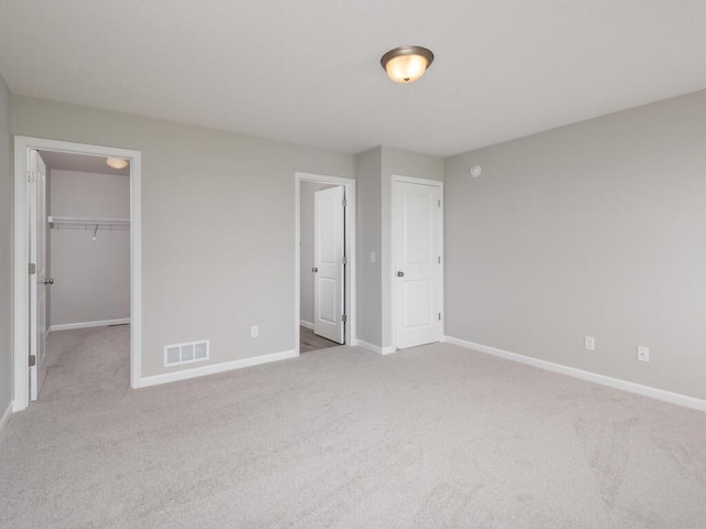 unfurnished bedroom featuring light colored carpet, a spacious closet, and a closet