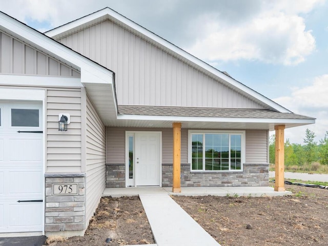 entrance to property with a garage, stone siding, a porch, and a shingled roof