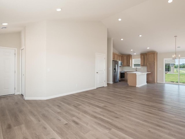 unfurnished living room featuring baseboards, light wood-style floors, high vaulted ceiling, a notable chandelier, and recessed lighting