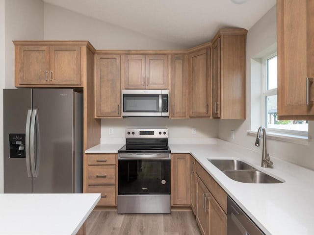 kitchen with lofted ceiling, stainless steel appliances, a sink, light wood-style floors, and light countertops