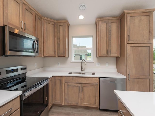 kitchen with stainless steel appliances, light countertops, visible vents, brown cabinetry, and a sink