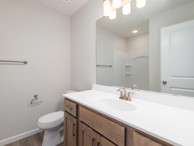 bathroom featuring a shower, toilet, vanity, wood finished floors, and baseboards