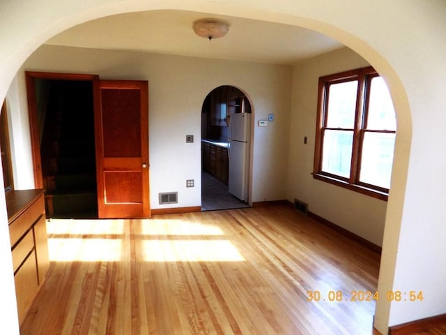 empty room with arched walkways, baseboards, visible vents, and light wood-type flooring