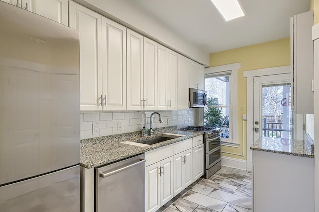 kitchen with light stone countertops, backsplash, appliances with stainless steel finishes, sink, and white cabinets