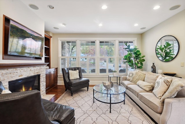 living room with built in shelves, light wood-type flooring, and a stone fireplace