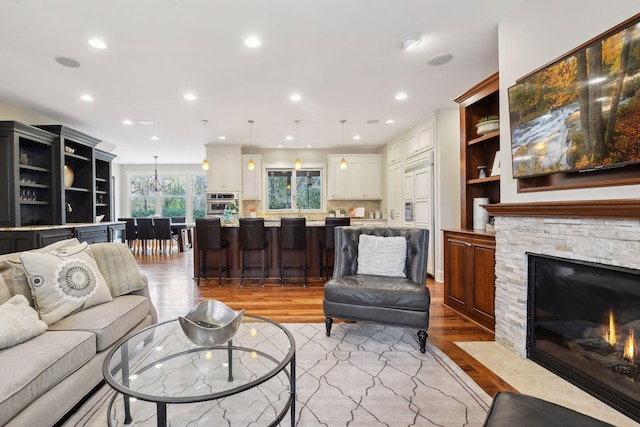 living room featuring light hardwood / wood-style floors, built in features, and a stone fireplace