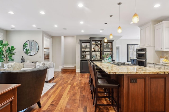 kitchen featuring appliances with stainless steel finishes, light stone counters, a kitchen island, white cabinetry, and decorative light fixtures