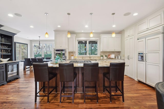 kitchen with light stone counters, dark hardwood / wood-style floors, decorative light fixtures, a kitchen island, and beverage cooler