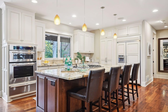 kitchen with a kitchen breakfast bar, double oven, pendant lighting, a kitchen island, and white cabinetry