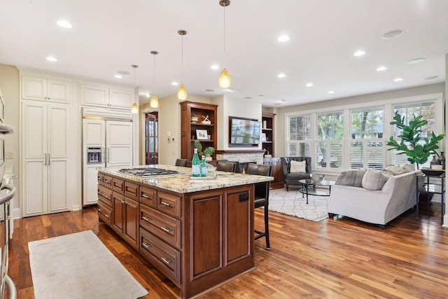 kitchen with decorative light fixtures, stainless steel gas cooktop, hardwood / wood-style floors, a breakfast bar area, and a kitchen island