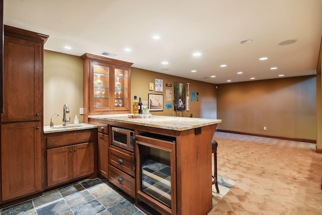 bar with light stone counters, stainless steel microwave, wine cooler, and sink