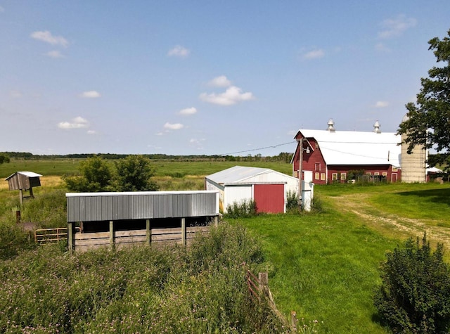 view of yard featuring driveway, a detached garage, a rural view, an outbuilding, and fence