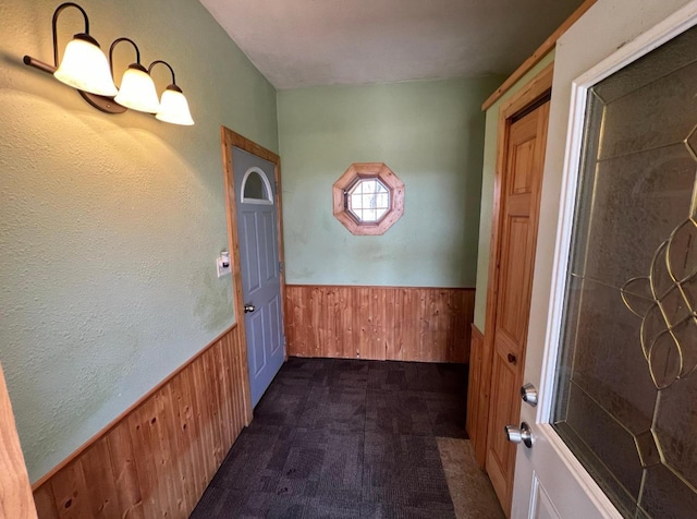 doorway featuring wainscoting, dark carpet, and wooden walls