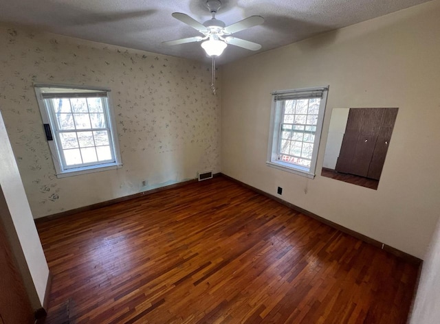 unfurnished room with a wealth of natural light, hardwood / wood-style floors, visible vents, and baseboards