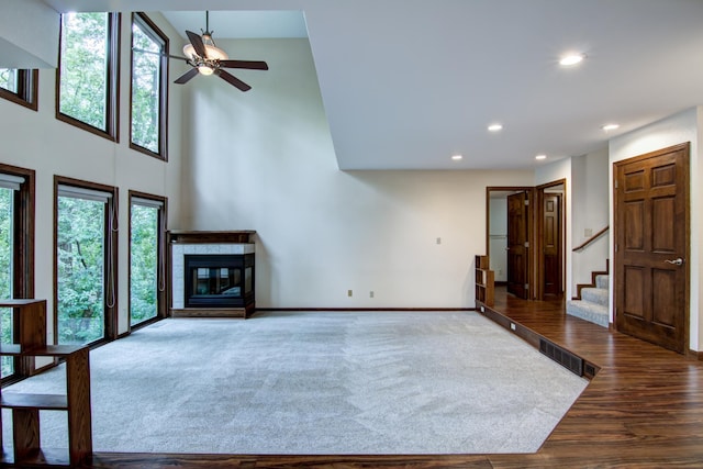 unfurnished living room with a towering ceiling, a tiled fireplace, ceiling fan, and hardwood / wood-style flooring